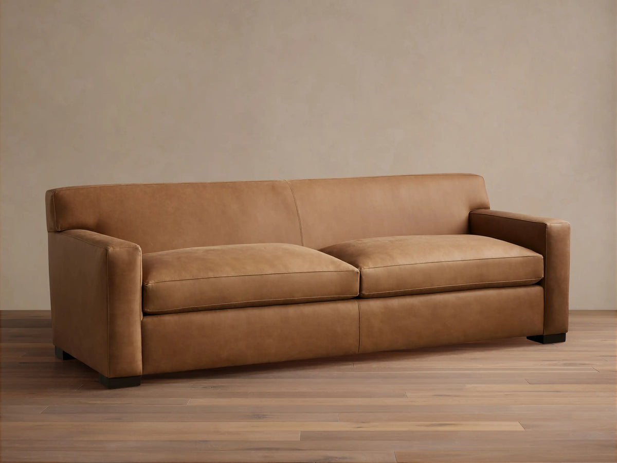 Bronte Leather Sofa in brown leather with a sleek design, featuring straight arms and deep seat cushions on a hardwood floor.