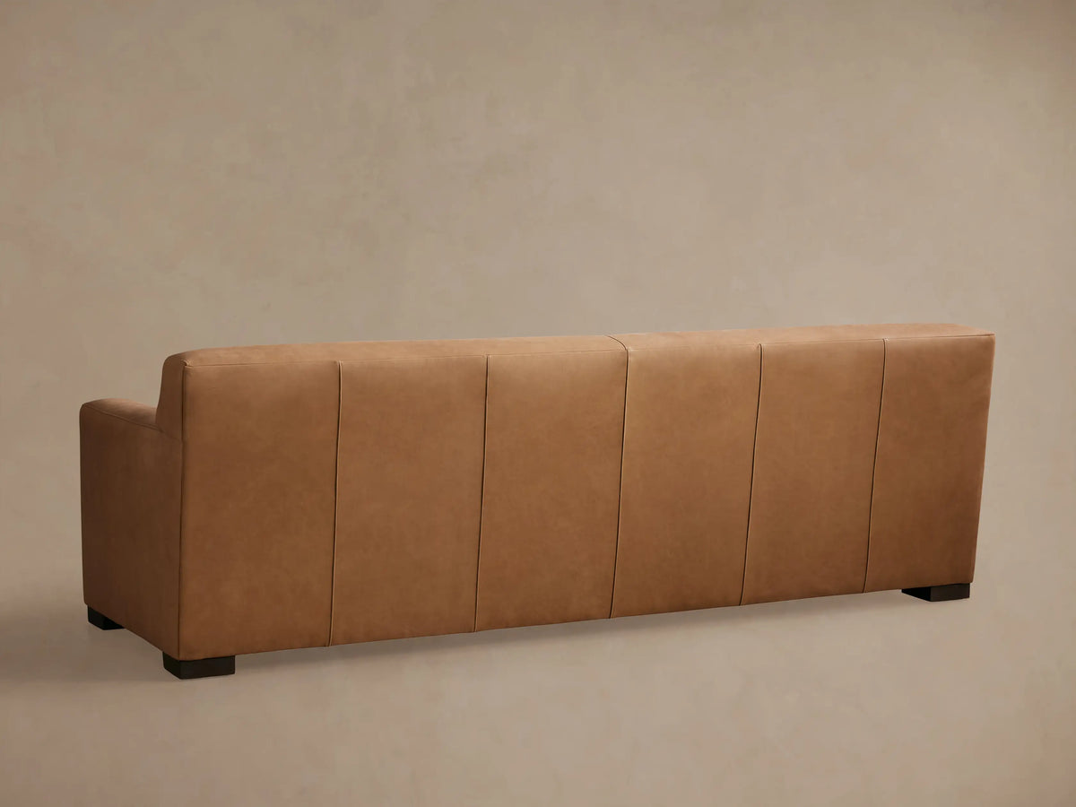 Bronte Leather Sofa in tan leather, featuring a plush backrest and armrest, with visible stitching and dark wood legs.