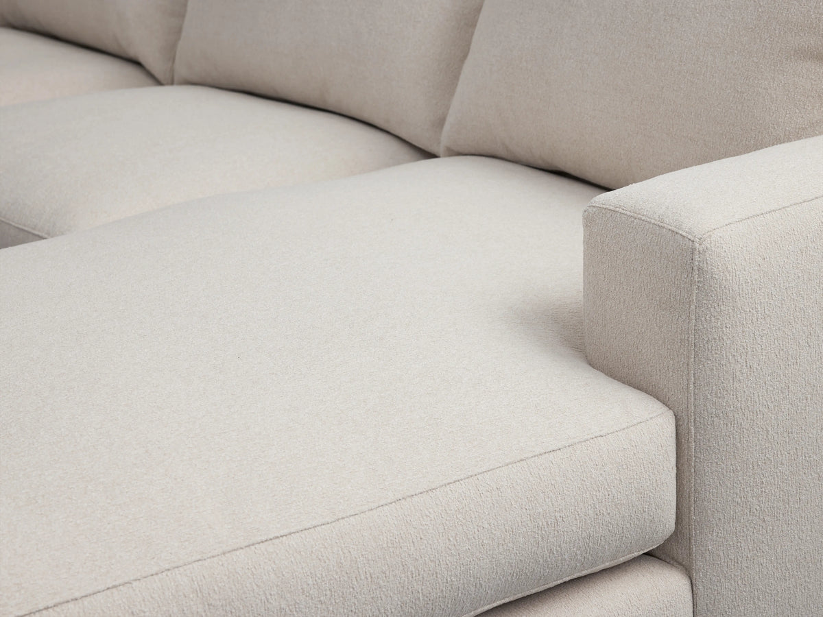 Close-up of Zarevium Dune Chaise Sectional, showing soft, textured light beige fabric seat, chaise extension, and rectangular right armrest.