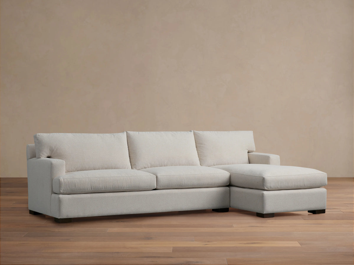 Zarevium Dune light off-white two-piece chaise sectional on wood floor, tan wall backdrop.