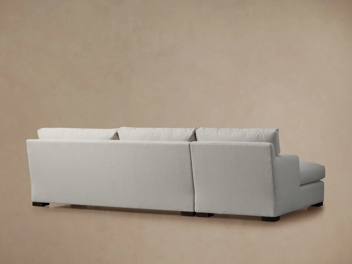 Zarevium Dune Two-Piece Chaise Sectional with light fabric, seen from the back-right. Dark feet visible on a neutral background.