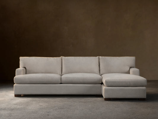 Zarevium Dune Two-Piece Chaise Sectional in light cream fabric, chaise on left, on a wood floor against a beige wall.