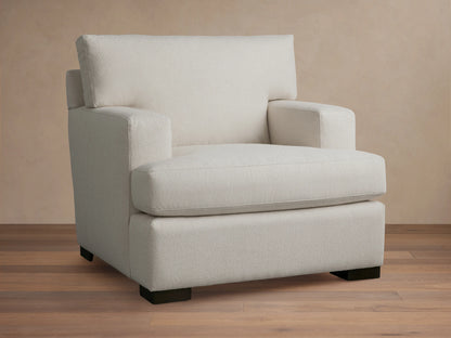 White Dune Chair with square arms and cushioned seat and backrest. Features a minimalistic design with dark wooden legs on a wooden floor.