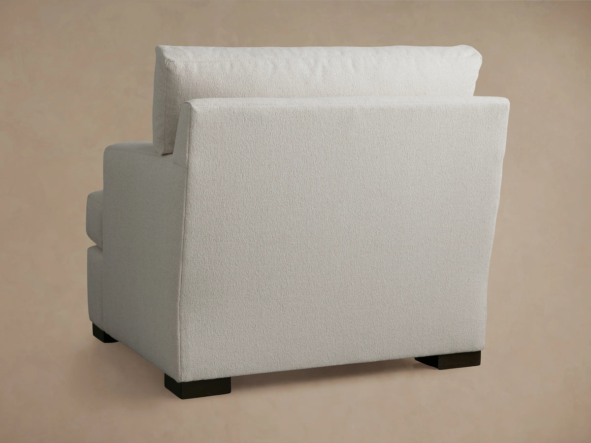 Dune Chair in neutral fabric, showing a close-up of the cushioned armrest and angled backrest against a soft beige background.