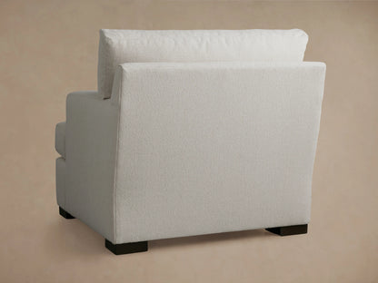 Dune Chair in neutral fabric, showing a close-up of the cushioned armrest and angled backrest against a soft beige background.