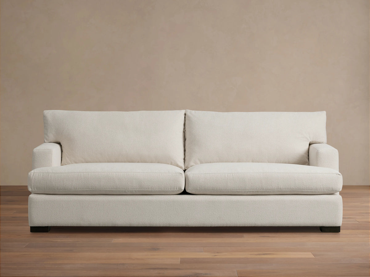 Dune Sofa in a neutral beige fabric, featuring a clean-lined design with plush back and seat cushions, and sturdy square arms, on a wooden floor.
