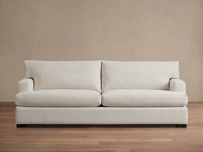 Dune Sofa in a neutral beige fabric, featuring a clean-lined design with plush back and seat cushions, and sturdy square arms, on a wooden floor.