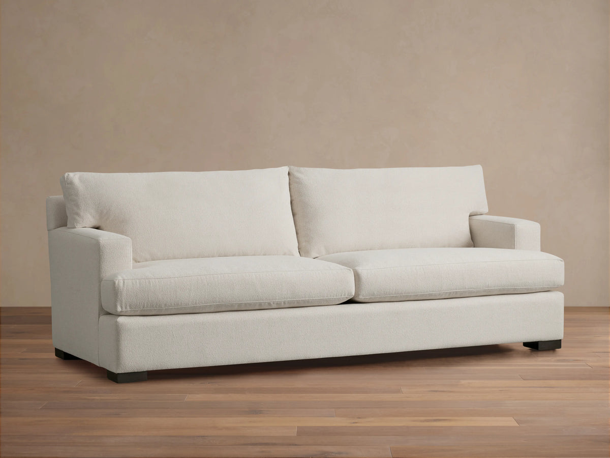 Dune Sofa in a neutral beige fabric, featuring a clean-lined design with plush back and seat cushions, and sturdy square arms, on a wooden floor.