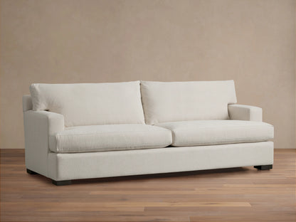 Dune Sofa in a neutral beige fabric, featuring a clean-lined design with plush back and seat cushions, and sturdy square arms, on a wooden floor.