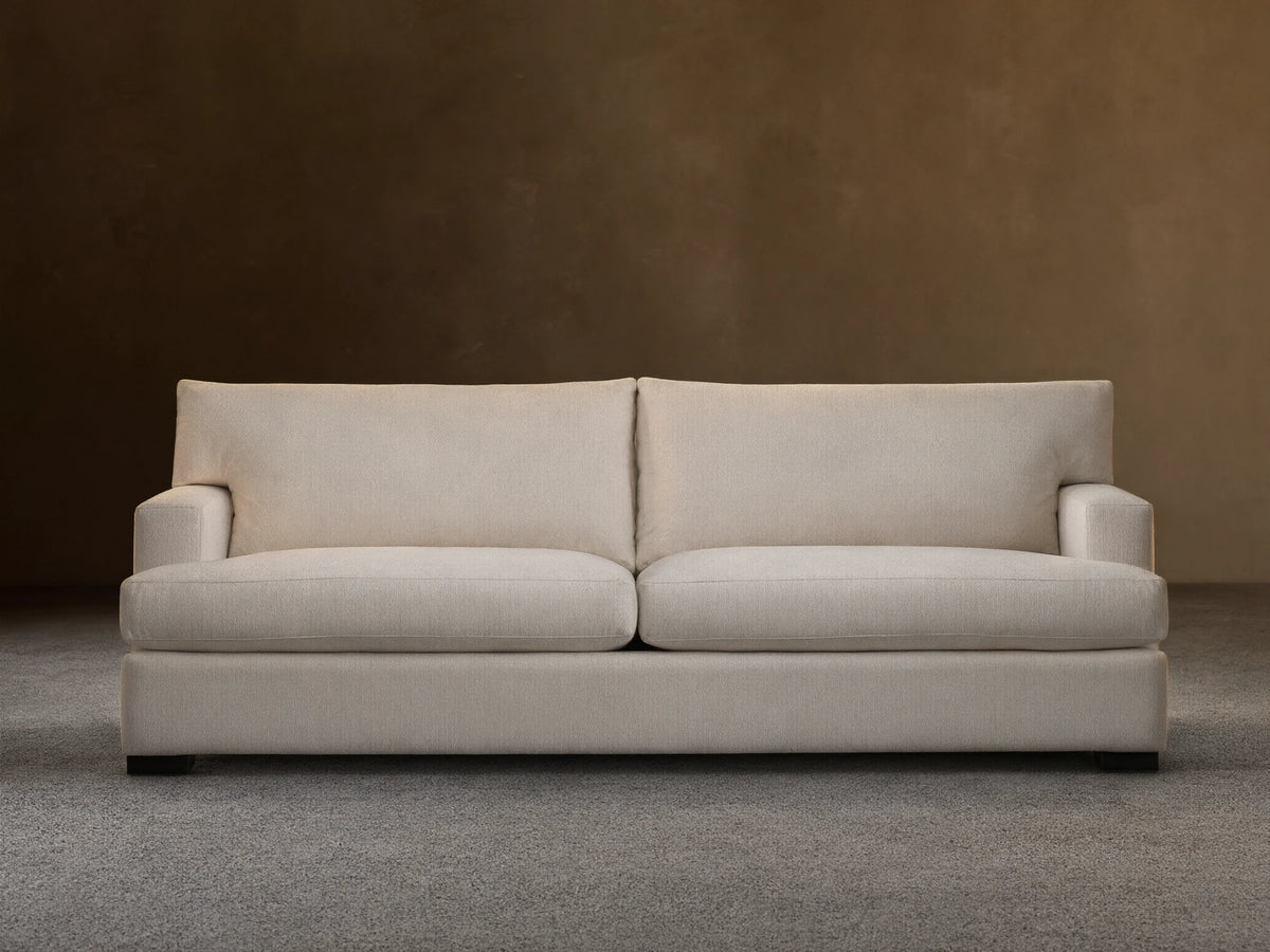 Dune Sofa in a neutral beige fabric, featuring a clean-lined design with plush back and seat cushions, and sturdy square arms, on a wooden floor.