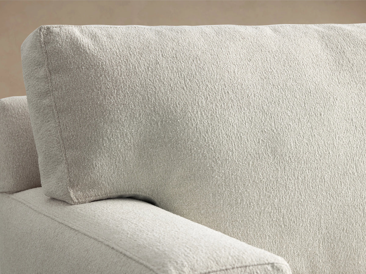 A light beige Dune Sofa with a minimalist design on a wooden floor, featuring plush cushions and sturdy armrests.