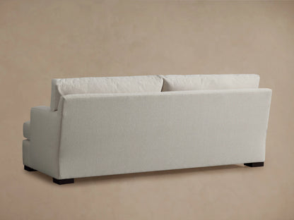 The image shows a close-up of the Dune Sofa's corner, highlighting its soft, textured, light-colored fabric and plush cushioning.
