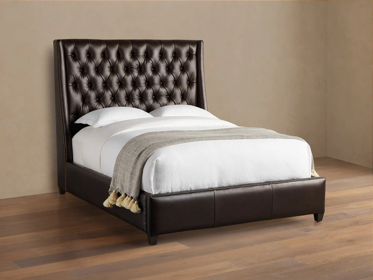 Devereaux Leather Tufted Bed in dark brown leather with a deeply tufted headboard, white bedding, and gray throw on wood floor.