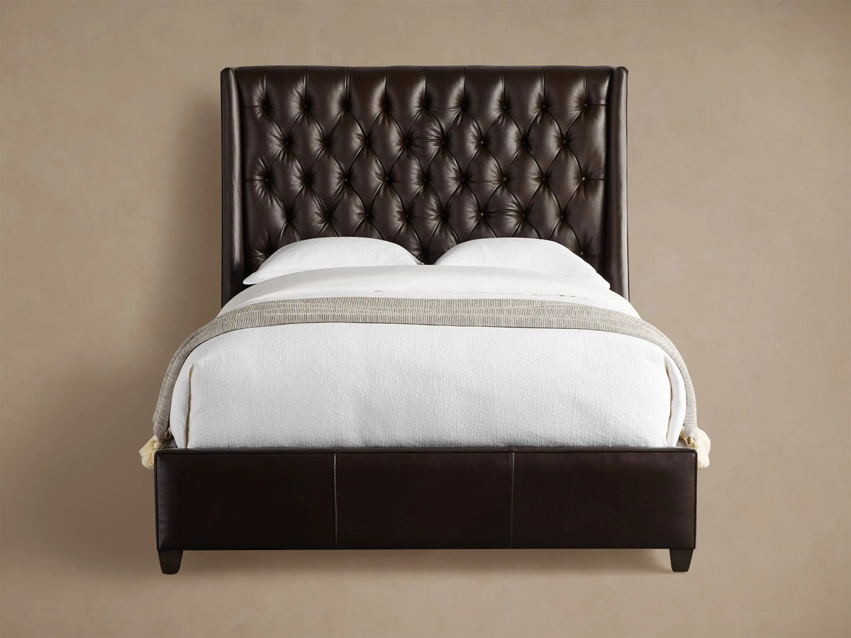 Devereaux Leather Tufted Bed in dark brown leather with a deeply tufted headboard, white bedding, and gray throw on wood floor.