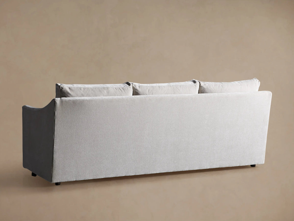 Close-up of the Branson Sofa, featuring its light grey textured fabric seat cushion and curved backrest, against a beige wall.