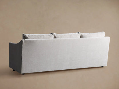Close-up of the Branson Sofa, featuring its light grey textured fabric seat cushion and curved backrest, against a beige wall.