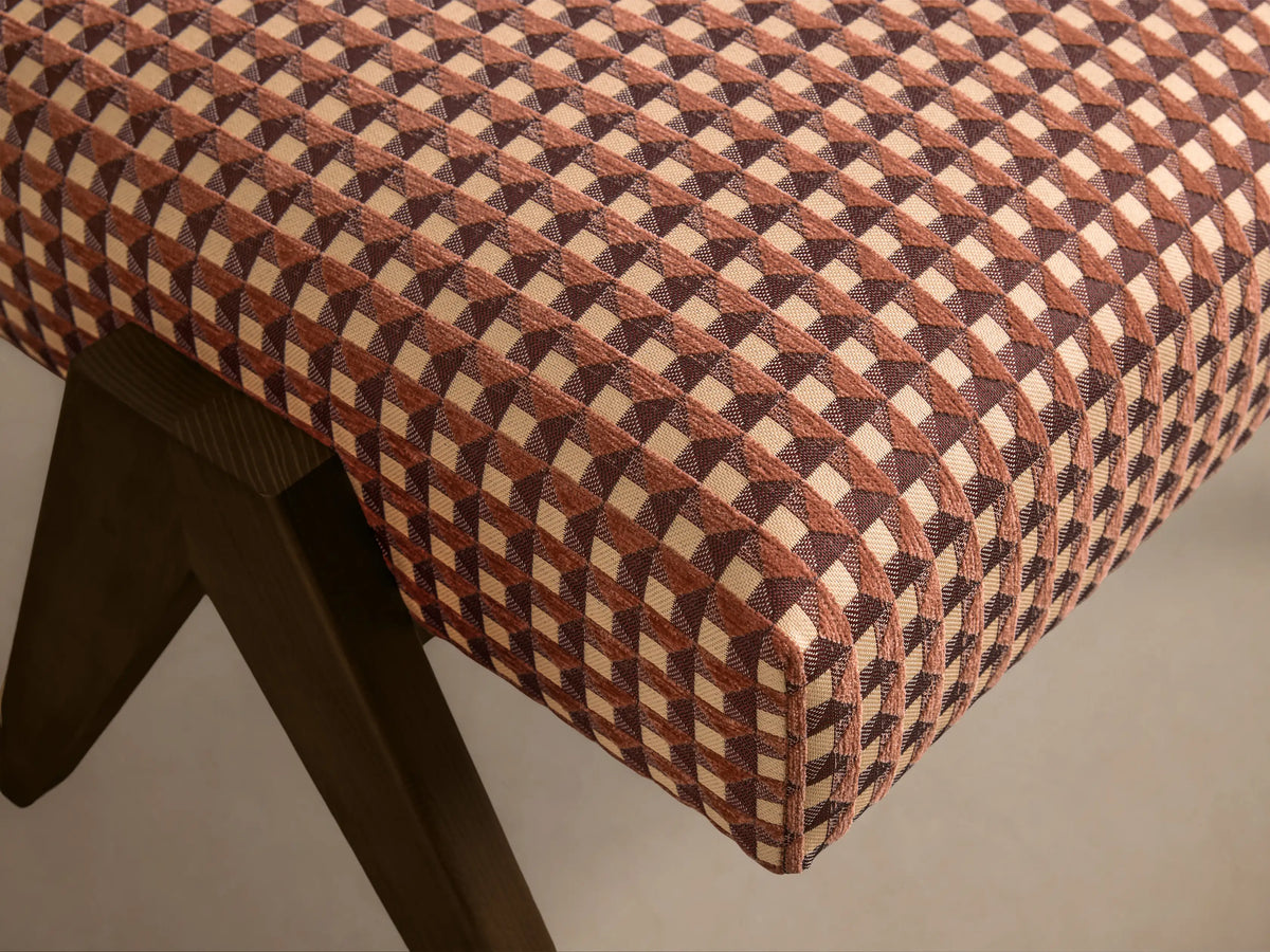 Close-up of the Elias Ottoman, showing a brown and beige geometric checkered upholstery with dark wooden legs.