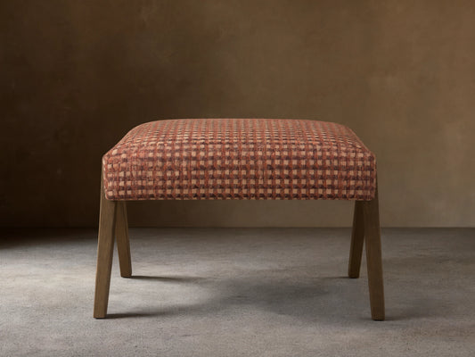 Front view of the Elias Ottoman with reddish-brown, light brown, and dark brown geometric cube pattern upholstery and light wood legs.