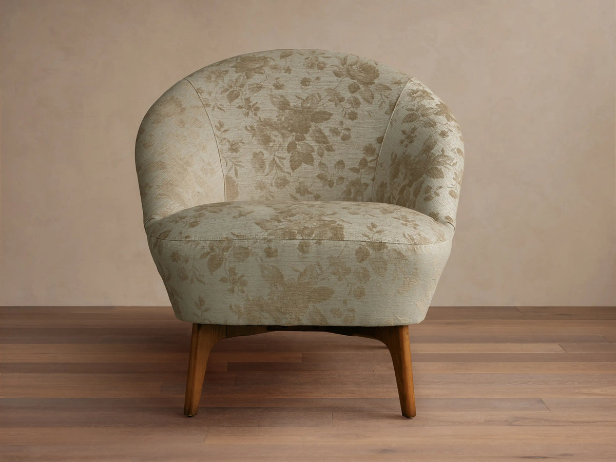 Front view of the light beige Elodie Chair, armless with a rounded back, subtle fabric pattern, and dark wood legs.