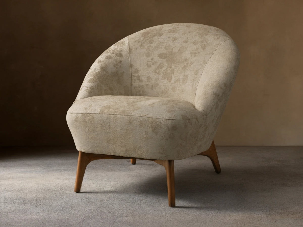 Front view of the beige floral Elodie Chair with a rounded back and tapered wooden legs.
