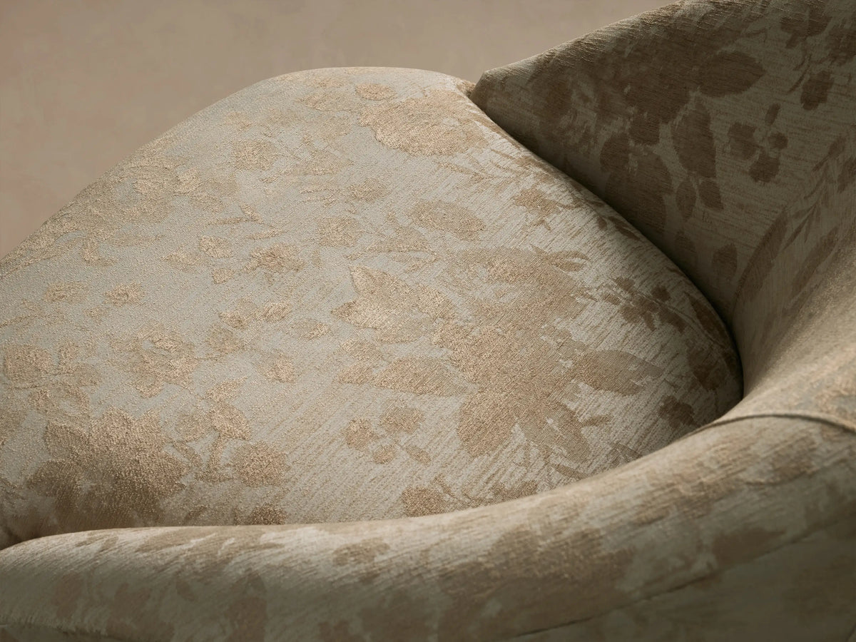 Front view of the Elodie Chair with light beige upholstery and a tan floral pattern, featuring a rounded barrel-back and four tapered wooden legs.