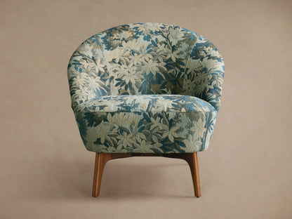 Front view of the light beige upholstered Elodie Chair with a subtle floral pattern, curved back, and dark wood legs.