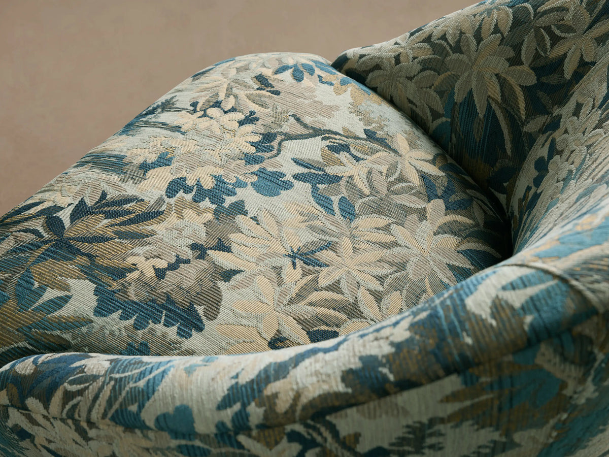 Elodie Chair: Curved barrel armchair in blue, green, and cream botanical fabric, with tapered wooden legs, front view.