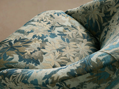 Elodie Chair: Curved barrel armchair in blue, green, and cream botanical fabric, with tapered wooden legs, front view.