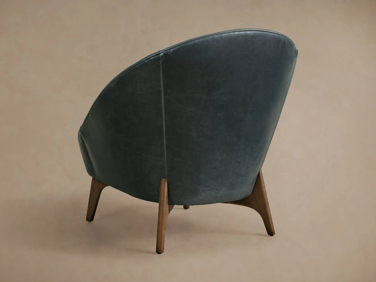 Elodie Leather Chair close-up, showcasing smooth, dark leather upholstery with curved stitching and cushioned seat back in soft lighting.