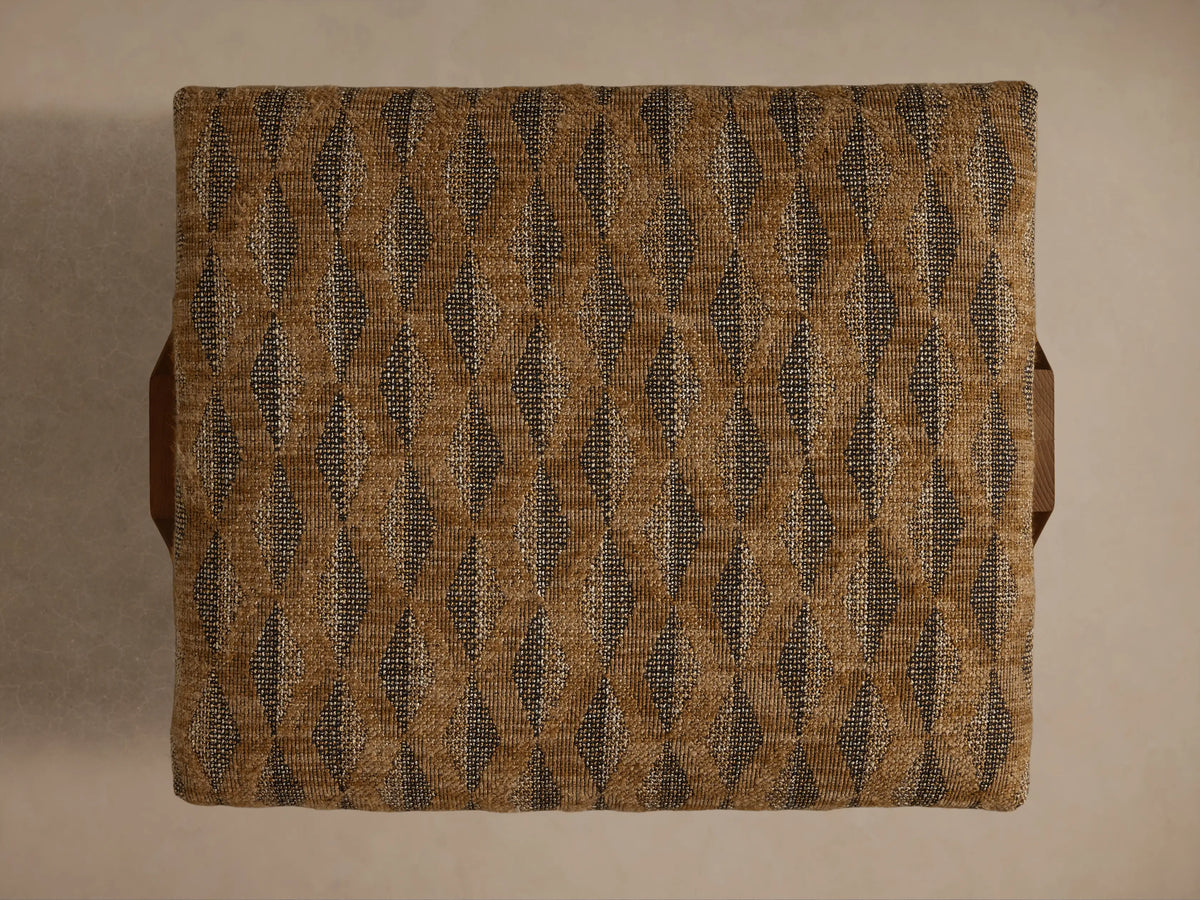 Close-up of the Elias Ottoman, featuring beige and brown woven geometric fabric upholstery and a light brown wooden leg.