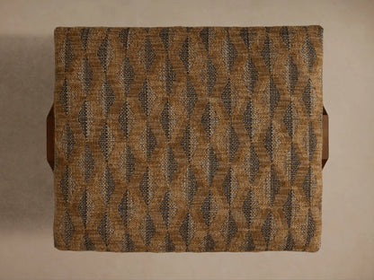 Close-up of the Elias Ottoman, featuring beige and brown woven geometric fabric upholstery and a light brown wooden leg.