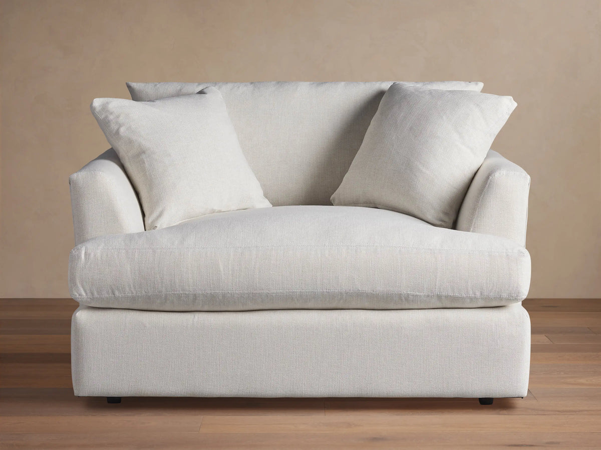 Emory Chair: Large armchair in light, textured fabric, with a deep seat, wide arms, and two soft back pillows. Neutral setting.