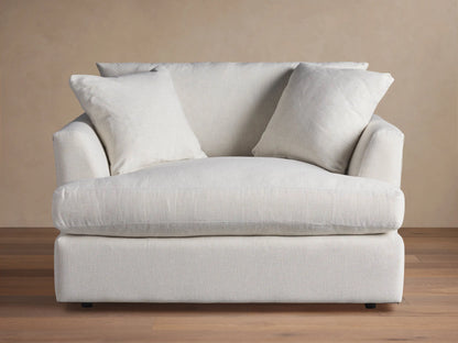 Emory Chair: Large armchair in light, textured fabric, with a deep seat, wide arms, and two soft back pillows. Neutral setting.