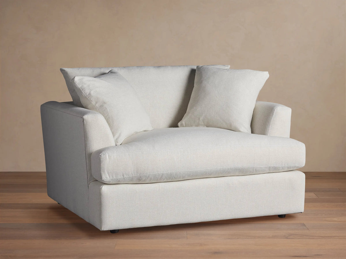 Emory Chair: Large armchair in light, textured fabric, with a deep seat, wide arms, and two soft back pillows. Neutral setting.
