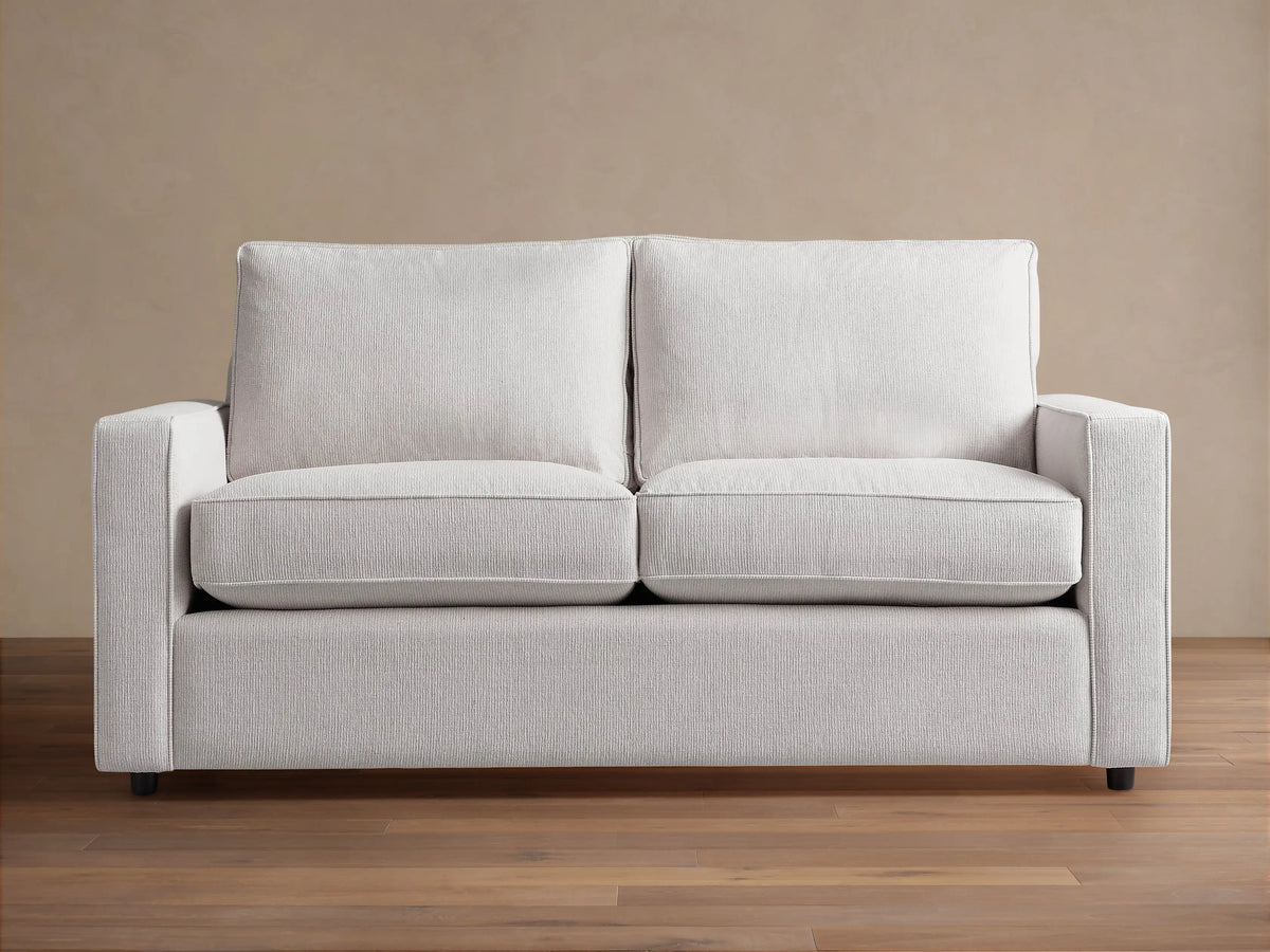 Filmore Air Sleeper Sofa: light gray two-seat sofa with square arms, textured fabric, on a wood floor.