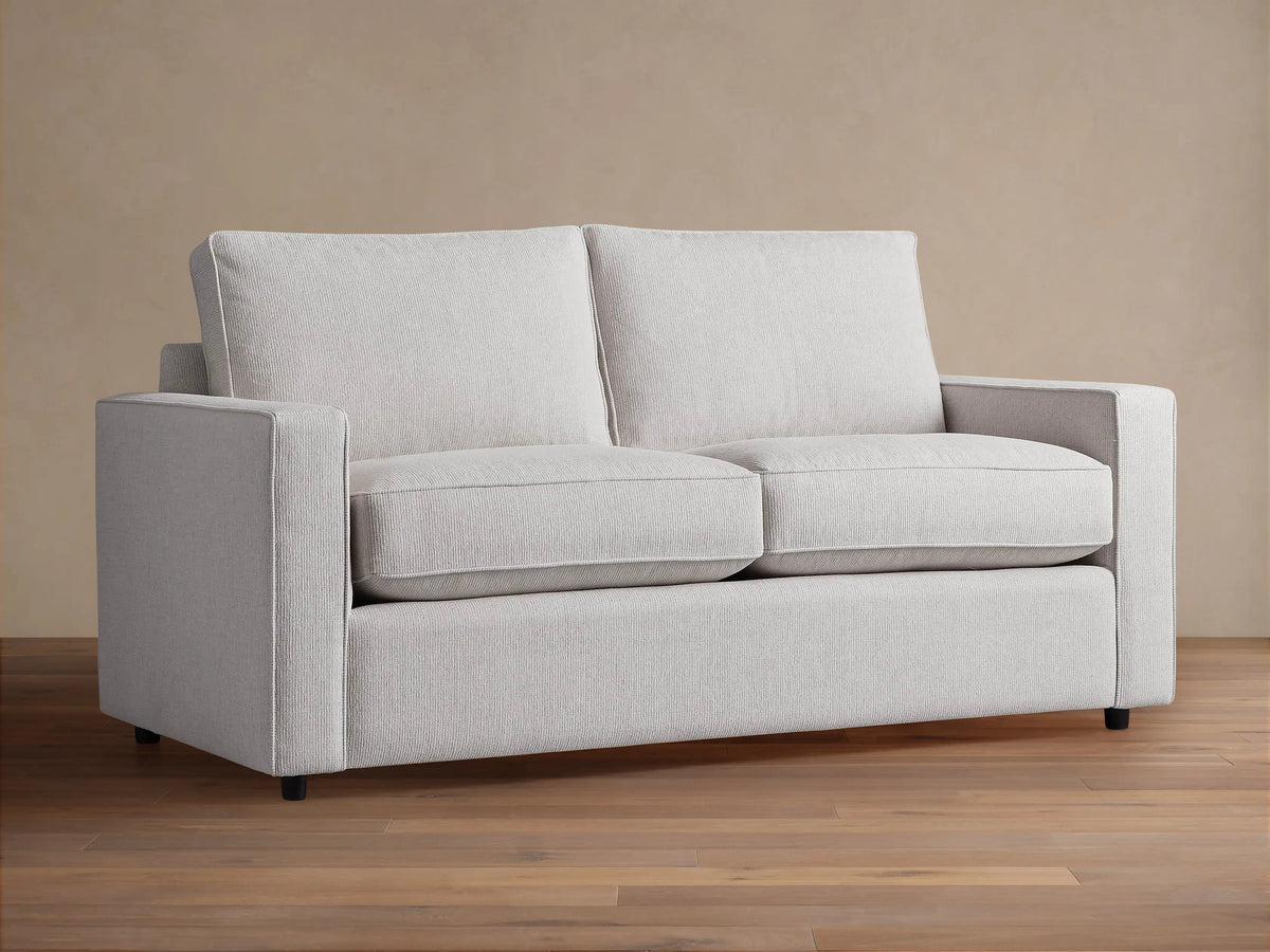 Filmore Air Sleeper Sofa: light gray two-seat sofa with square arms, textured fabric, on a wood floor.