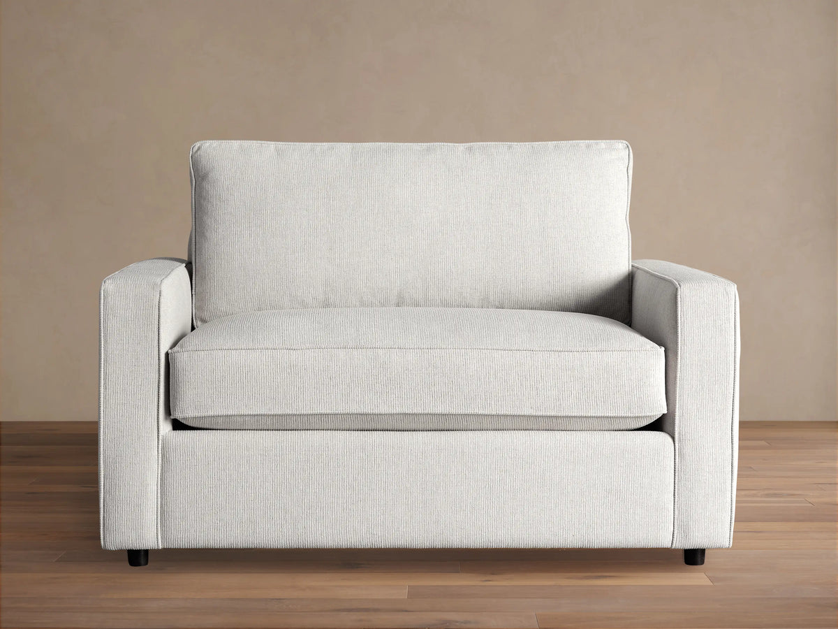 Filmore Twin Air Sleeper Chair, light gray textured fabric, front view, on wood floor against brown wall.
