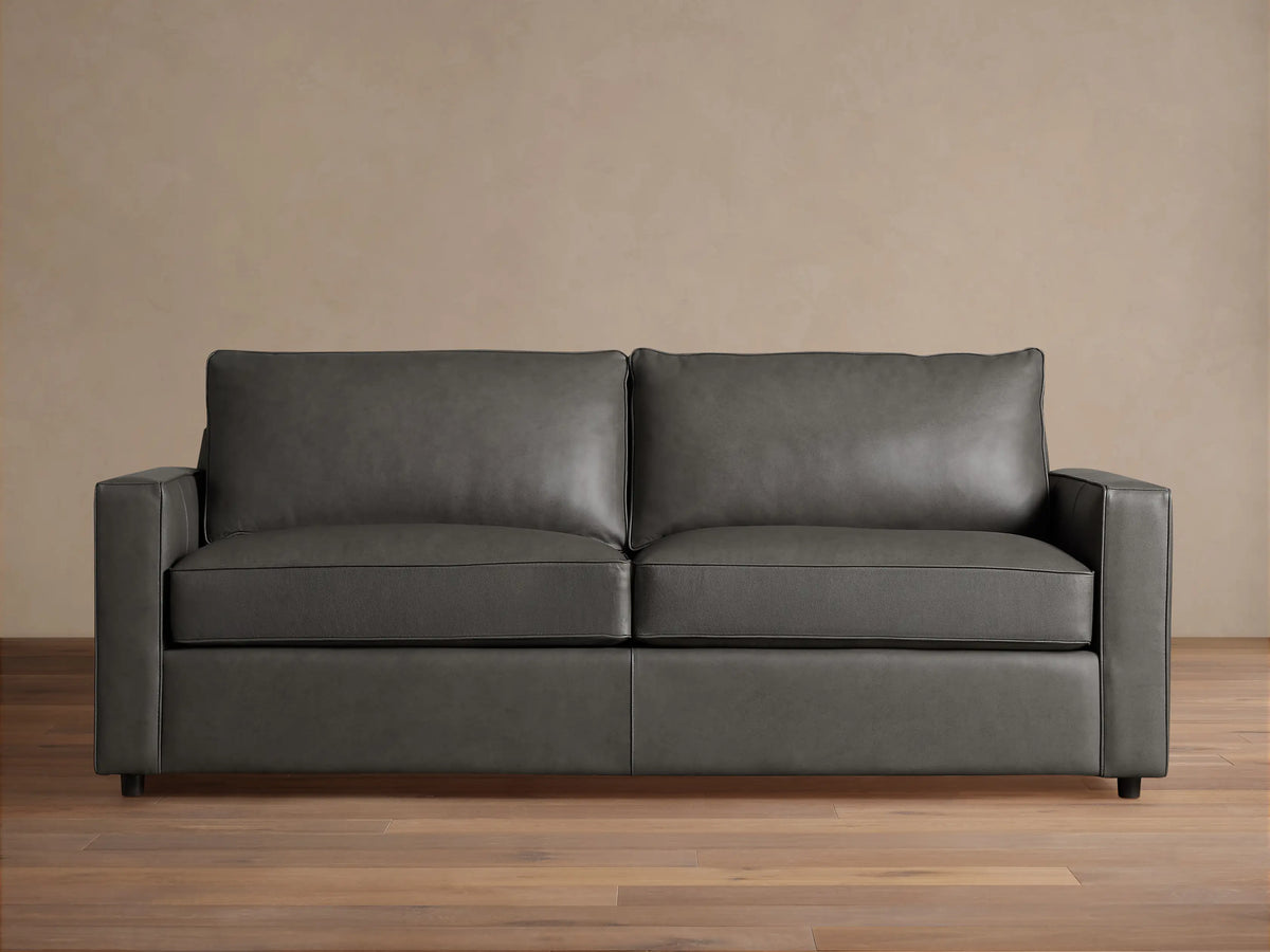 Dark gray Filmore Leather Air Sleeper Sofa, modern design with straight arms and piped cushions, against a neutral wall and wood floor.
