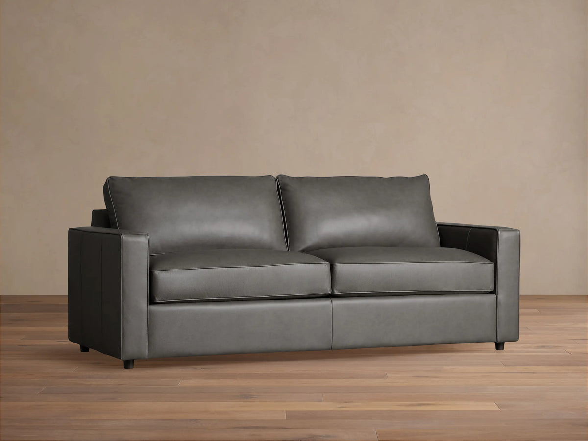 Dark gray Filmore Leather Air Sleeper Sofa, modern design with straight arms and piped cushions, against a neutral wall and wood floor.
