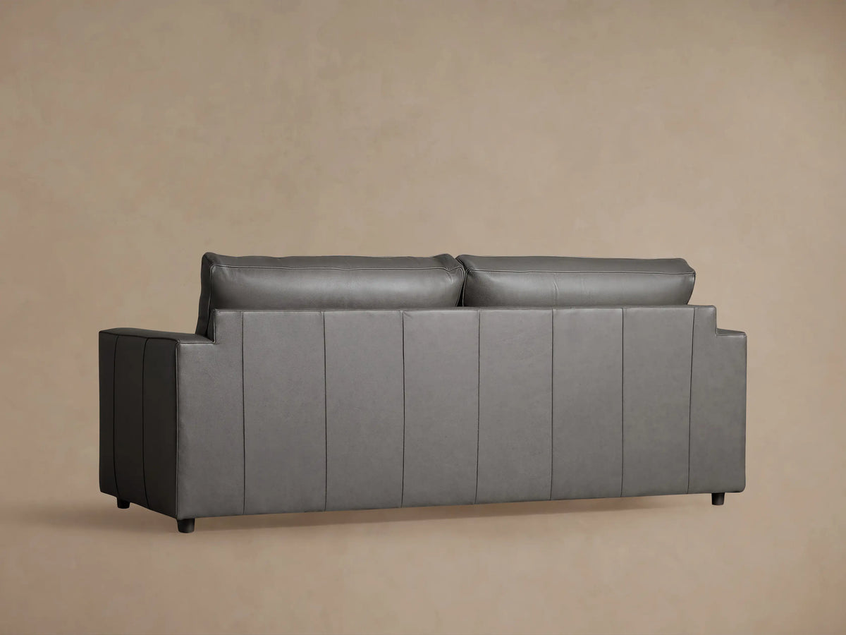 Close-up of Filmore Leather Air Sleeper Sofa, showing a dark grey leather squared armrest and seat cushion with piping.
