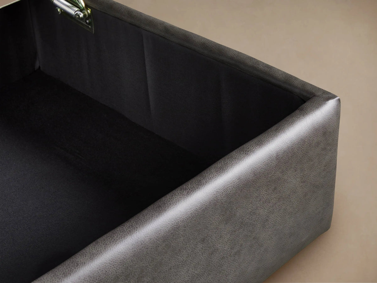 Filmore Leather Storage Ottoman, charcoal, rectangular, with two parallel top seams and castors, on wood floor.