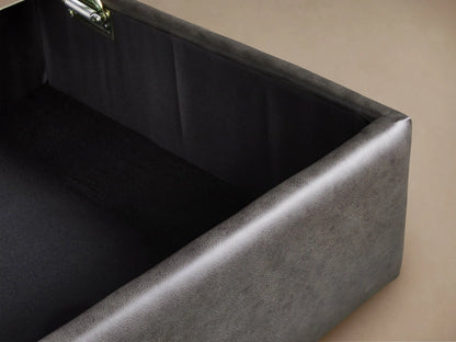 Filmore Leather Storage Ottoman, charcoal, rectangular, with two parallel top seams and castors, on wood floor.