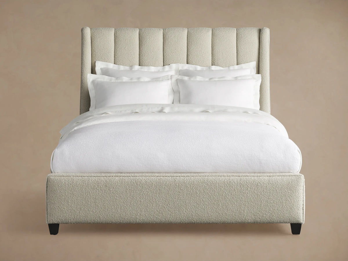 Hayworth Bed: Light beige textured upholstery, channel-tufted headboard, white bedding, dark feet, on wood floor.