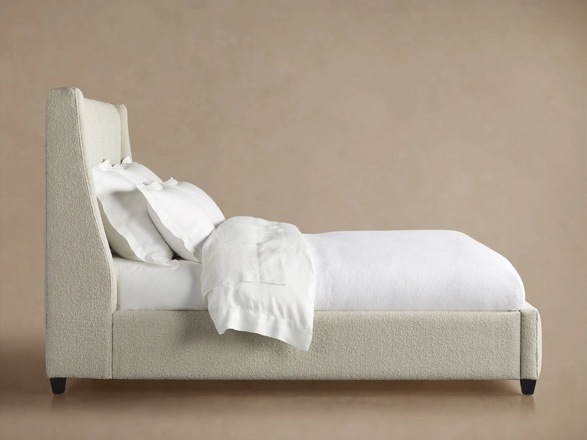 Hayworth Bed: Close-up of light beige, textured, channel-tufted headboard with white pillows, against a warm neutral wall.
