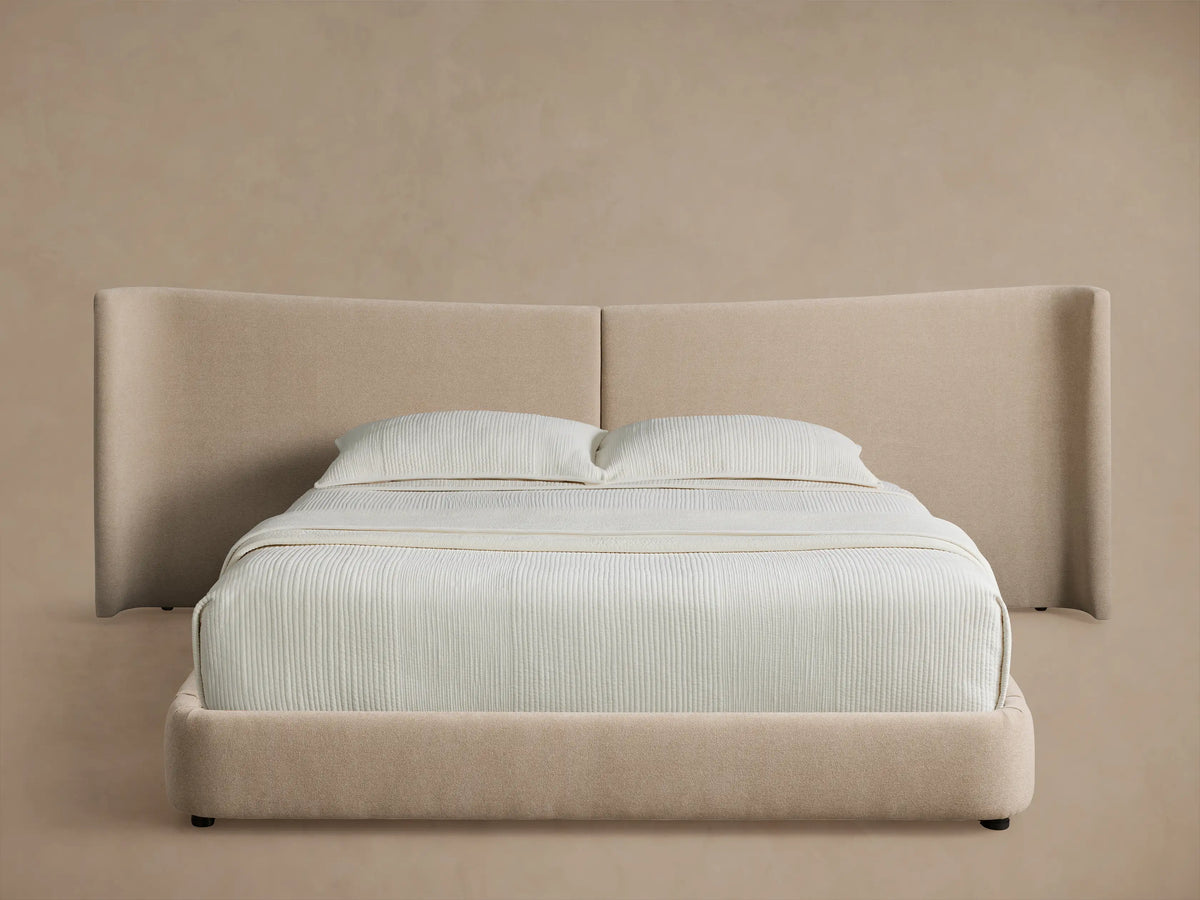 Hathaway Extended Bed: Light beige upholstered platform bed with extended winged headboard and white striped bedding.