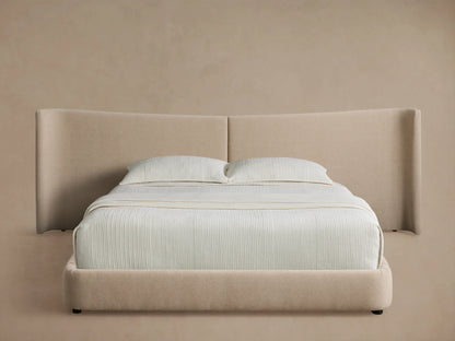 Hathaway Extended Bed: Light beige upholstered platform bed with extended winged headboard and white striped bedding.