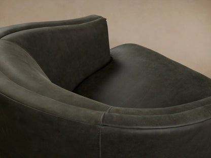 Dark green Kieran Leather Swivel Chair with a rounded backrest and cushioned seat, shown on wooden floor against a beige wall.