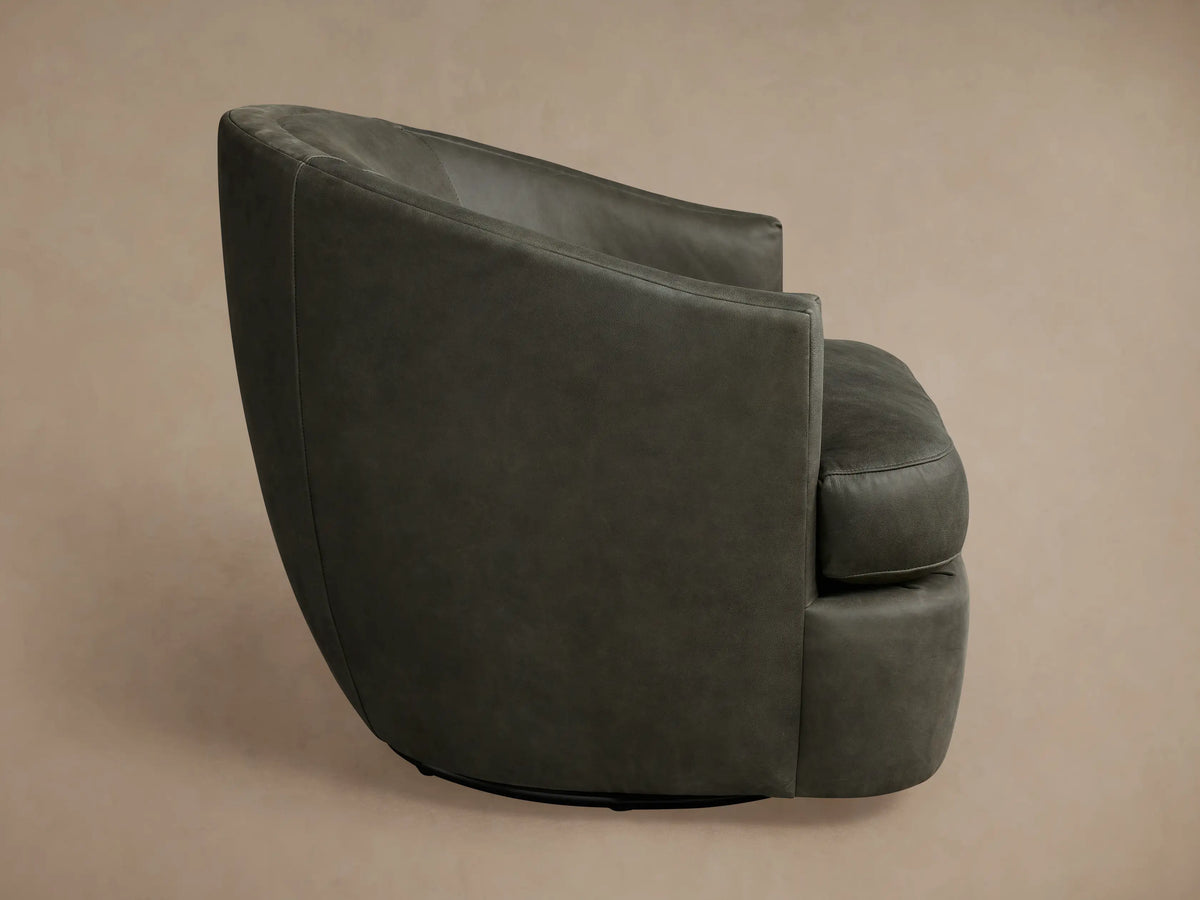 Kieran Leather Swivel Chair in dark grey, featuring a curved backrest and smooth leather texture, positioned at a three-quarter angle.