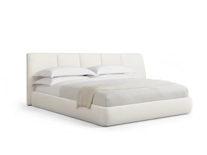 A modern cream-colored bed with a low profile and wide cushioned headboard, set against a beige wall, on wooden flooring.