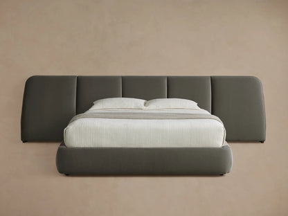 A modern bed with a dark gray upholstered frame and a large cushioned headboard. The bed is neatly made with a white sheet and two pillows.
